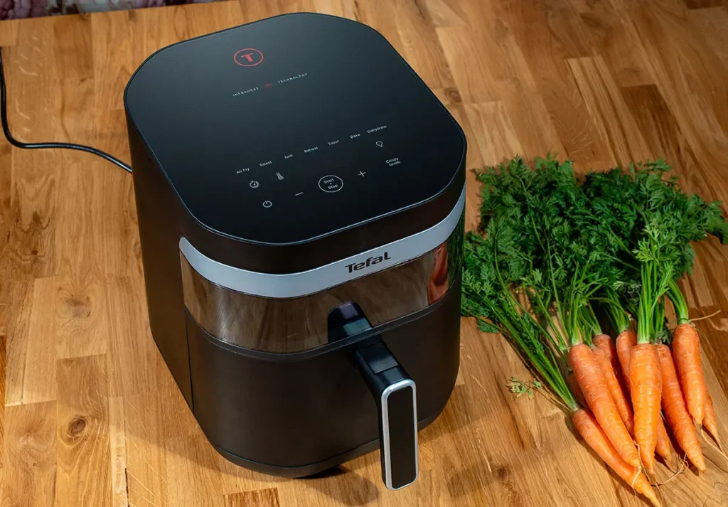 Tefal Easy Fry Infrared EY8328 - frytkownica beztłuszczowa z technologią podczerwieni na drewnianym blacie obok świeżych marchewek