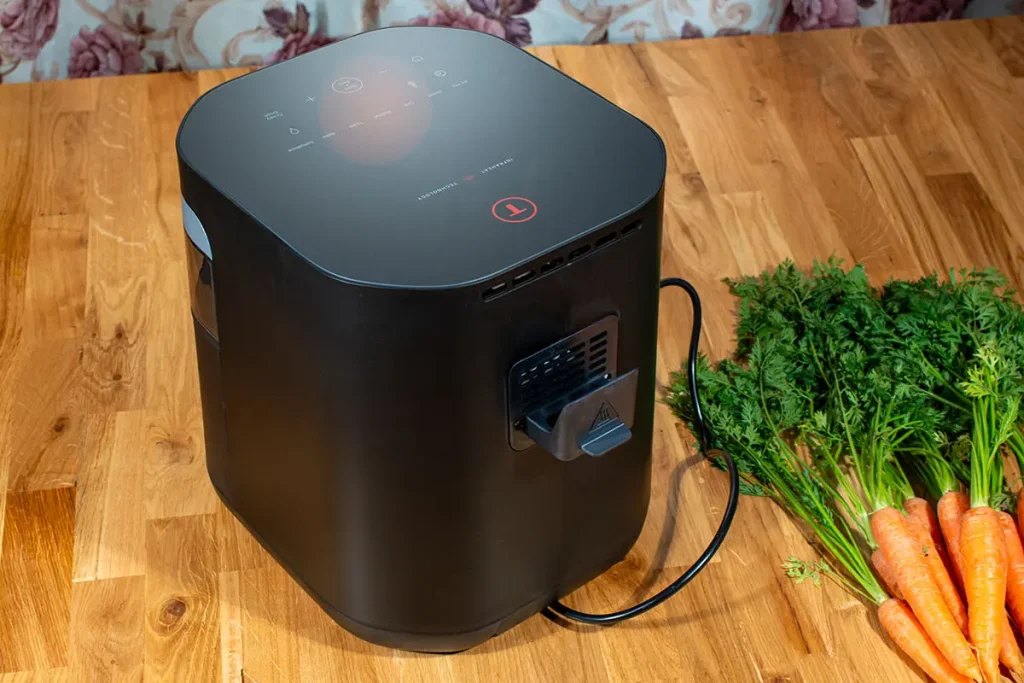 Tefal Easy Fry Infrared EY8328 widok z tyłu - kratka wentylacyjna, przewód zasilający i panel dotykowy od góry na drewnianym blacie obok świeżych marchewek