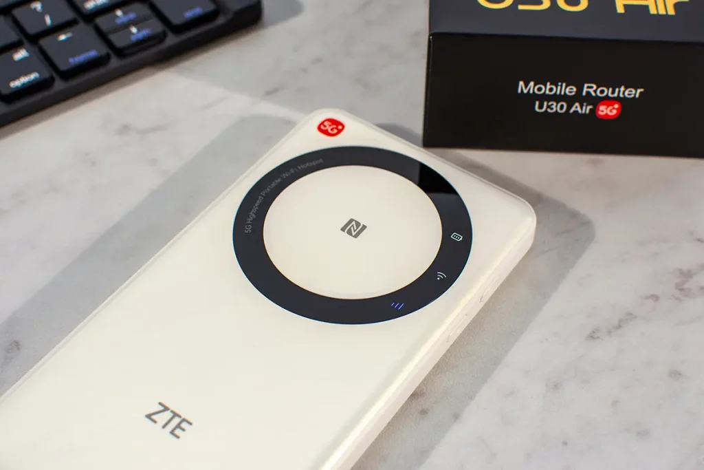 ZTE U30 Air – mobilny router 5G na biurku obok pudełka; widoczny okrągły panel z NFC i ikonami statusu (recenzja).